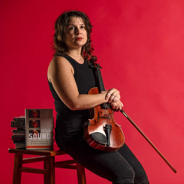 Amy Cimini sitting down and holding violin with her book as props