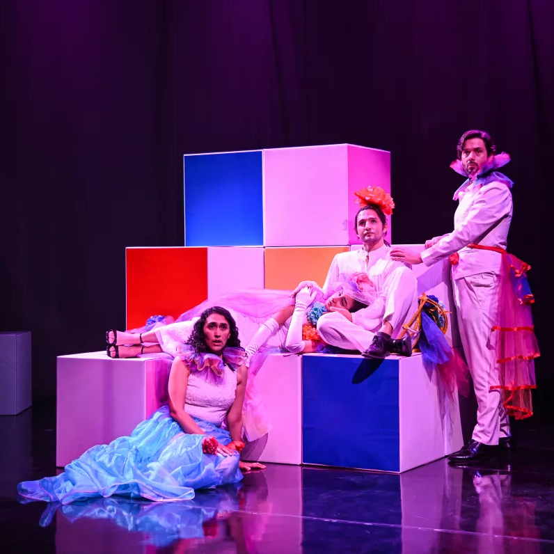 Natalia Merlano Gómez, Miguel Zazueta, and Jonathan Nussman wear white costumes, with colorful accents, and sing onstage